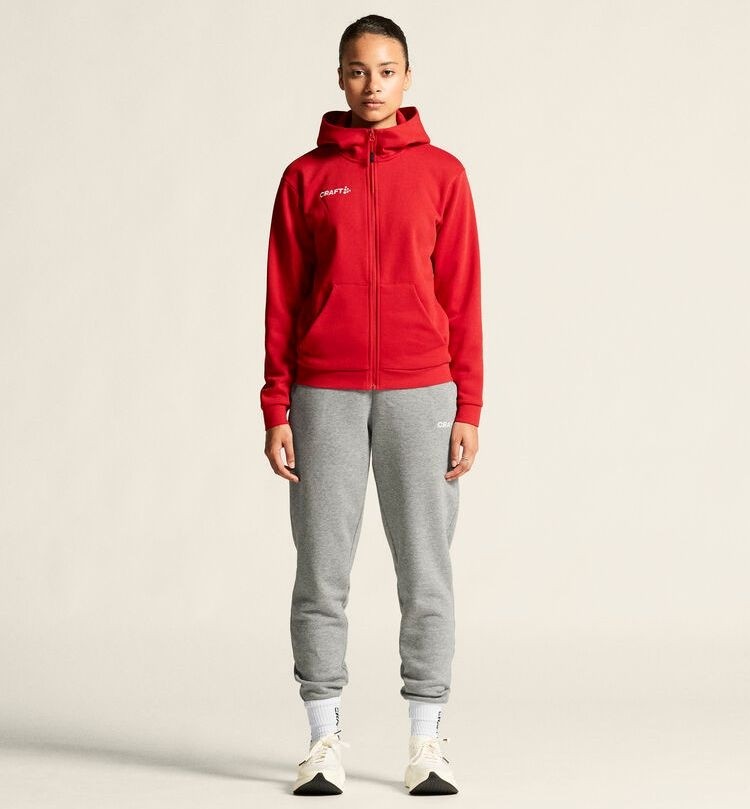 Damski dres bawełniany Craft Community 2.0 – czerwona bluza z kapturem zapinana na zamek oraz jasnoszare spodnie dresowe ze ściągaczami.