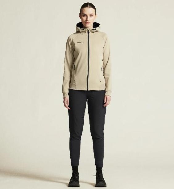 Damski dres tenisowy z linii premium Craft ADV Unify – beżowa rozpinana bluza z kapturem i czarne spodnie sportowe o dopasowanym fasonie.