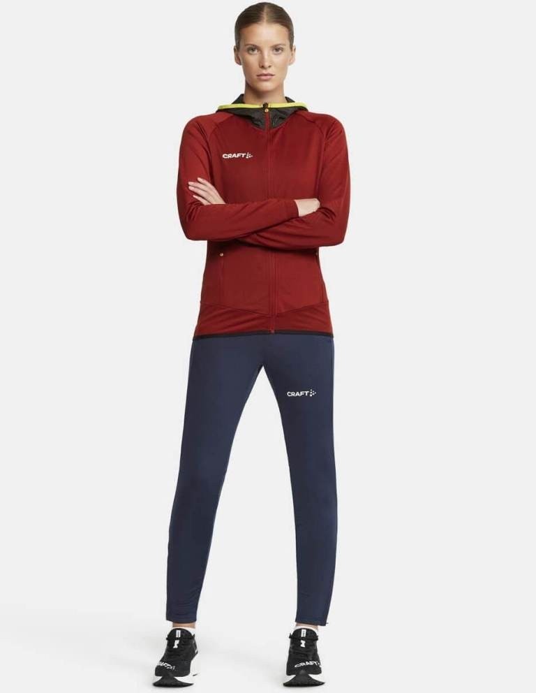 Kobieta w profesjonalnym dresie treningowym CRAFT Extend – bordowa bluza z kapturem i zamkiem oraz granatowe spodnie sportowe.
