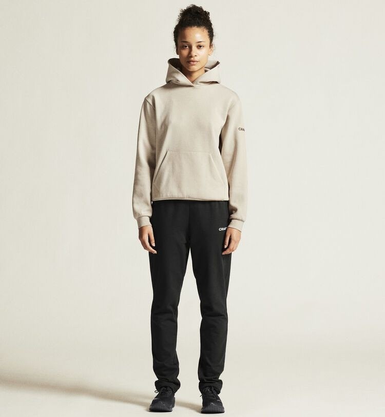 Damski dres bawełniany Craft Community 2.0 – kremowa bluza typu hoodie z kapturem i czarne spodnie dresowe z białym logo Craft na biodrze.