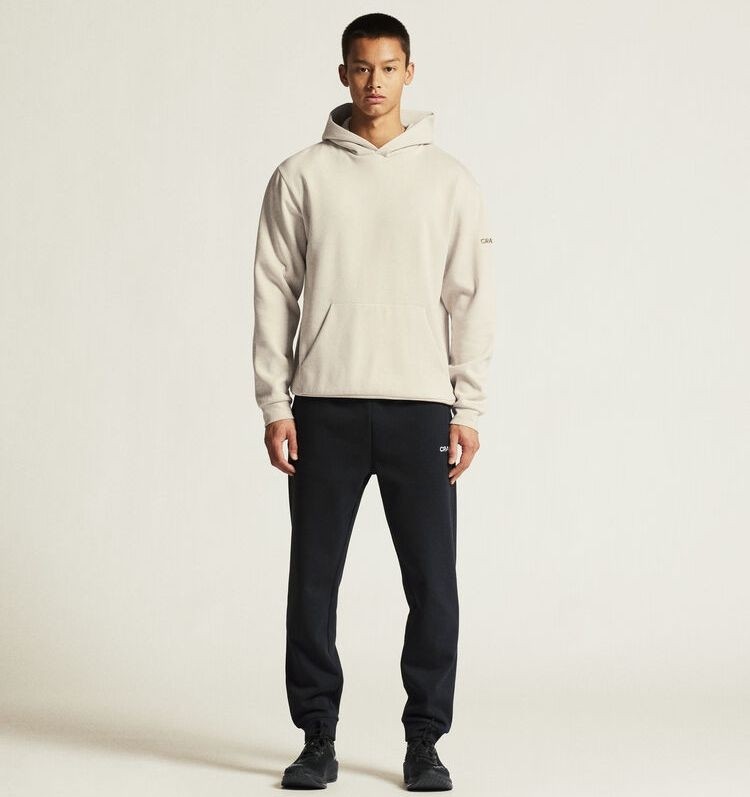 Męski dres bawełniany Craft Community 2.0 – biała bluza z kapturem typu hoodie oraz klasyczne czarne spodnie dresowe ze ściągaczami.