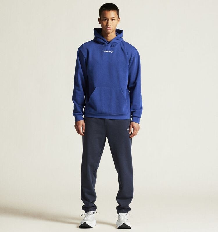 Męski dres bawełniany Craft Community 2.0 – niebieska bluza z kapturem wkładana przez głowę i granatowe spodnie dresowe ze ściągaczami.